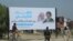 Iraqis walk by a poster announcing the upcoming visit of Pope Francis and his planned meeting with prominent Shiite Muslim leader, Ayatollah Ali al-Sistani, in Najaf, Iraq, March 3, 2021.