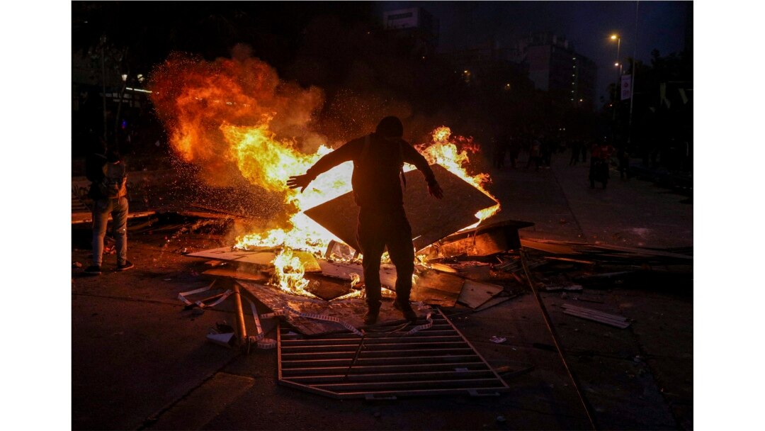 A wet anti-government protester dries his clothes by standing close to a burning street barricade, after police used a water cannon to disperse demonstrators in Santiago, Chile, Oct. 29, 2019.