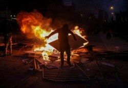 A wet anti-government protester dries his clothes by standing close to a burning street barricade, after police used a water cannon to disperse demonstrators in Santiago, Chile, Oct. 29, 2019.