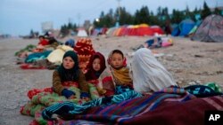 FILE - Afghan children are covered with a blanket as their families camp outside the Directorate of Disaster, in Herat, Afghanistan, Nov. 29, 2021.