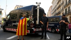 A woman with an ''estelada'' or Catalonia independence flag places a carnation on a vehicle belonging to police officers from Mossos d'Esquadra in Barcelona, Spain, Sept. 24, 2017.
