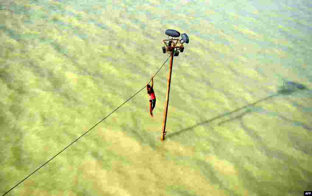 An Indian youth dangles from a power line before diving into the floodwaters of the overflowing Ganges river in Allahabad, Aug. 6, 2013. 