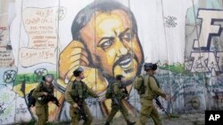 FILE - In the background of part of Israel's separation barrier with portrait of jailed Fatah leader Marwan Barghouti, Israeli soldiers patrol at Kalandia checkpoint between Jerusalem and the West Bank city of Ramallah, March 8, 2012