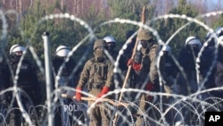Polish police and border guards stand near the barbed wire as migrants from the Middle East and elsewhere gather at the Belarus-Poland border near Grodno Grodno, Belarus, Nov. 9, 2021.