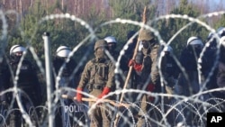 FILE - Polish police and border guards stand near the barbed wire as migrants from the Middle East and elsewhere gather at the Belarus-Poland border near Grodno Grodno, Belarus, Nov. 9, 2021.