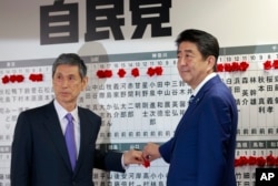 Japanese Prime Minister Shinzo Abe, right, leader of the Liberal Democratic Party, poses with vice president Masahiko Komura for photos as he marks on the name of one of those elected in the parliamentary lower house election at the party headquarters.