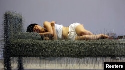 北京的周洁在行为艺术个展中躺在钢丝床上，有时裸睡