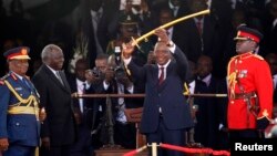 Uhuru Kenyatta (au c.) montre l'épée qu'il a reçue de son prédécesseur Mwai Kibaki comme l'un des symboles du pouvoir