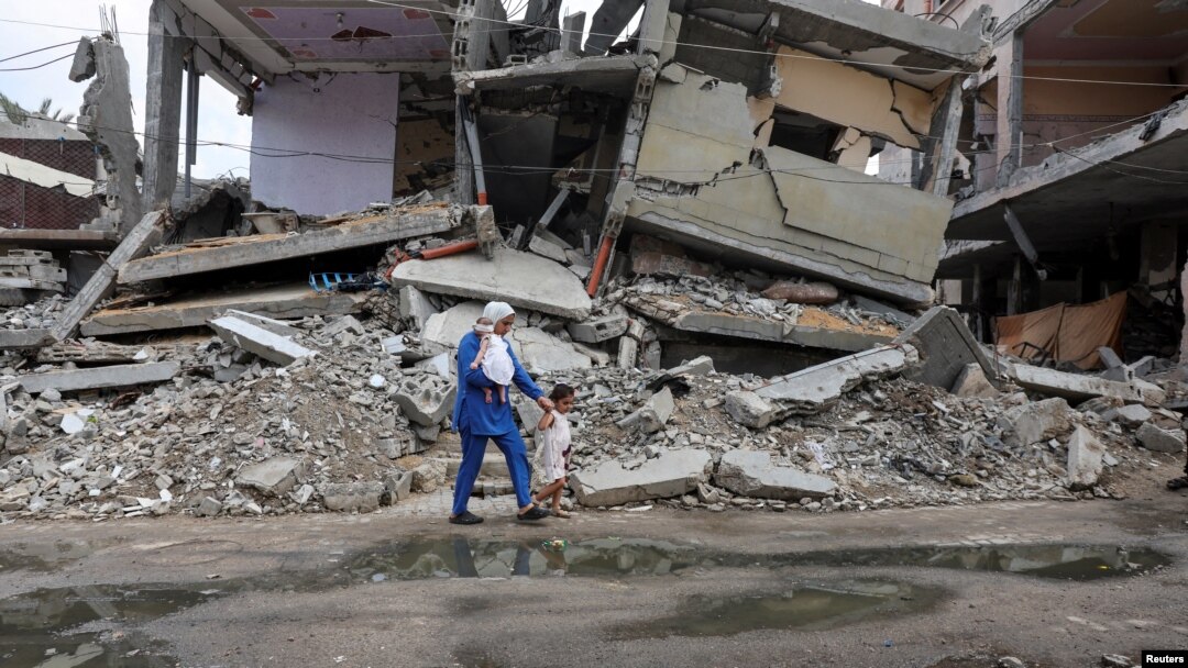 Wafaa Abdelhadi melintasi reruntuhan rumah yang hancur akibat serangan Israel bersama putrinya, Lynn dan Roueida, setelah vaksinasi polio di Deir Al-Balah, Gaza Tengah, 1 September 2024. (Foto: Ramadan Abed/Reuters)