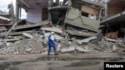 Wafaa Abdelhadi melintasi reruntuhan rumah yang hancur akibat serangan Israel bersama putrinya, Lynn dan Roueida, setelah vaksinasi polio di Deir Al-Balah, Gaza Tengah, 1 September 2024. (Foto: Ramadan Abed/Reuters)