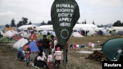 FILE - A banner placed by activists is seen on a street sign at a makeshift camp for refugees and migrants at the Greek-Macedonian border, near the village of Idomeni, Greece, March 17, 2016.