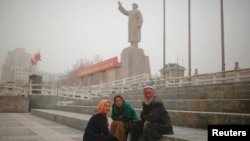 Ethnic Uighurs sit near a statue of China's late Chairman Mao Zedong in Kashgar, Xinjiang Uighur Autonomous Region, China, March 23, 2017. 