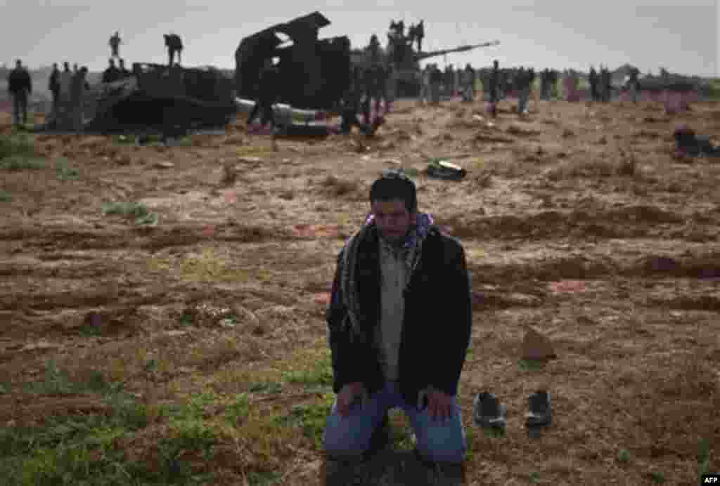 A Libyan man prays in front a destroyed tank on the outskirts of Benghazi, eastern Libya, Sunday, March 20, 2011. The U.S. military said 112 Tomahawk cruise missiles were fired from American and British ships and submarines at more than 20 coastal target