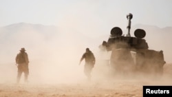 FILE - Hezbollah fighters walk near a military tank in Western Qalamoun, Syria, Aug. 23, 2017. 