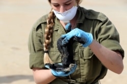 FILE - An Israeli soldier holds a clump of tar cleaned from the sand after an offshore oil spill deposited tar along Israel's Mediterranean shoreline, at a beach in Atlit, Israel, Feb. 22, 2021.