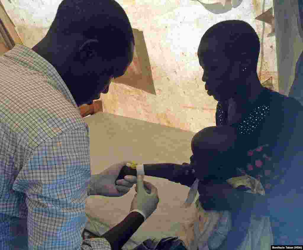 A health worker prepares to give medication intravenously to a South Sudanese child who has tested positive for malaria, in Ayilo refugee resettlement camp in Uganda 