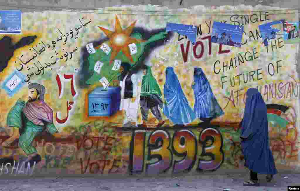 A woman walks past a wall with graffiti encouraging the public to vote in Kandahar province, Afghanistan, March 30, 2014.