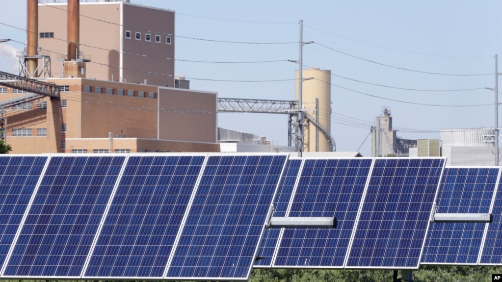资料照片：内布拉斯加州弗里蒙特的一组太阳能电池板，后面可见一家发电场。(2018年5月31日)(photo:VOA)