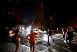 Pedestrians cross a dark street during a power outage, July 13, 2019, in New York.