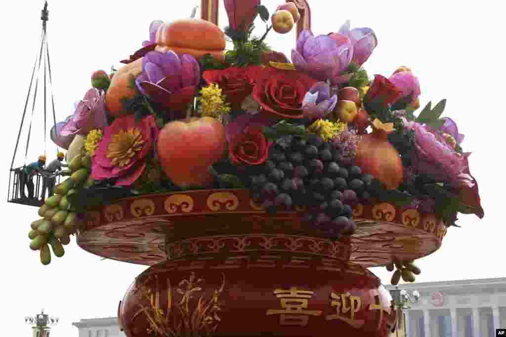 کارگران در حال تزئین یک سبد بزرگی از گل و میوه های مصنوعی در میدانی در چین می باشند که به مناسبت جشن روز ملی و جشنواره نیمه پاییز که در اواخر سپتامبر برگزار می شود.