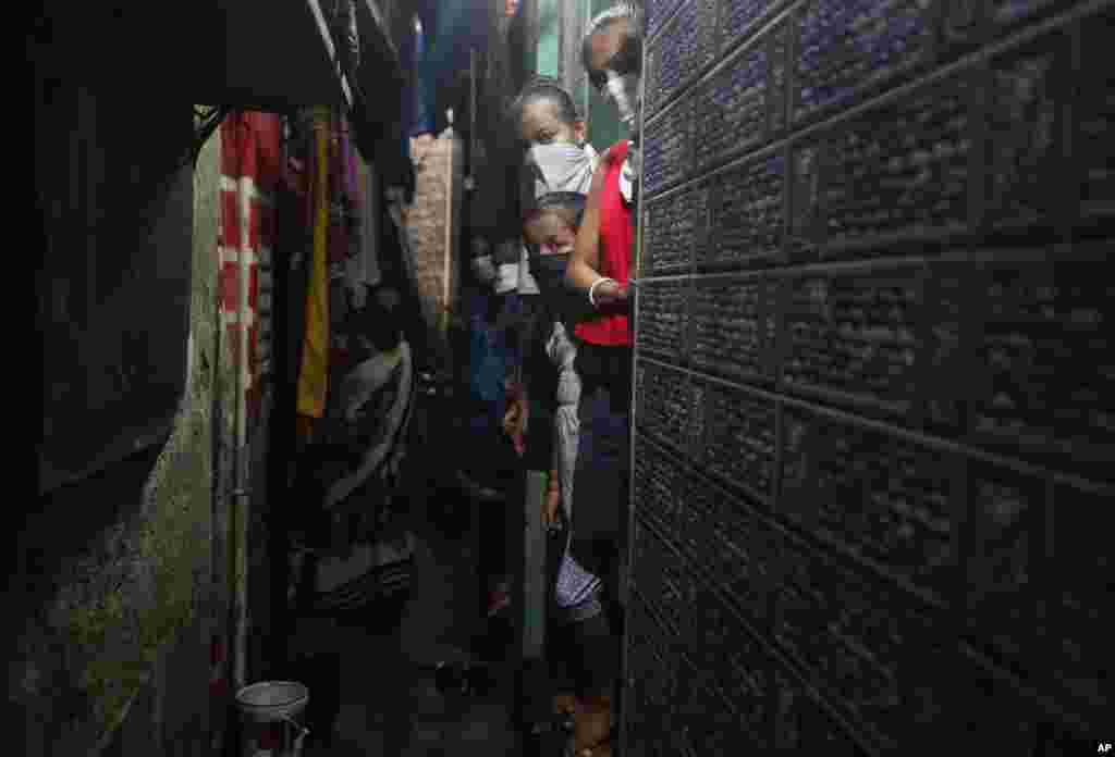 A group of children wearing masks look on as health workers examine people for signs of COVID-19, at a slum in Mumbai, India.