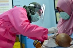 Seorang petugas medis mengenakan baju pelindung memberikan vaksinasi kepada seorang bayi di sebuah puskesmas di Banda Aceh, 18 Mei 2020. (Foto: AFP)