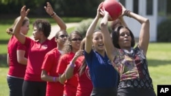 First lady Michelle Obama hands a ball to Olympic skater Michelle Kwan during an event in 2011 to promote physical fitness among military families