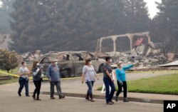 Carol Smith, far right in blue, her daughter Suzie Scatena, third from right, and husband Tim, third from left, tour their fire-ravaged neighborhood along with support crews, Aug. 2, 2018, in Redding, Calif. The Smiths' home of 30 years was destroyed by a wildfire.