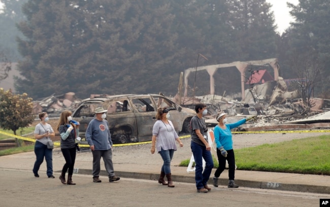 Carol Smith, far right in blue, her daughter Suzie Scatena, third from right, and husband Tim, third from left, tour their fire-ravaged neighborhood along with support crews, Aug. 2, 2018, in Redding, Calif. The Smiths' home of 30 years was destroyed by a wildfire.