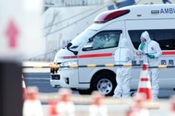 Officials in protective suits talk near the cruise ship Diamond Princess anchored at the Yokohama Port in Yokohama, south of Tokyo, Feb. 6, 2020.