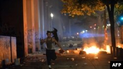 FILE - A man runs as several protesters manage to breach the fence and enter the portico of the Multnomah County Justice Center in Portland, Oregon, July 23, 2020. Protesters set fire to part of the complex Tuesday evening.