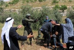 An Israeli soldier points his pistol at a group of Palestinians gathering around a wounded Osama Hajahjeh, 16, near the village of Tekoa, West Bank, Apri 18, 2019.