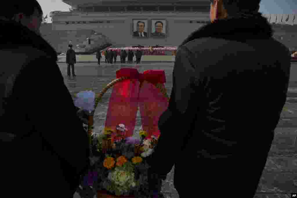 Warga Korea Utara bersiap menyimpan karangan bunga di bawah foto-foto mendiang pemimpin mereka Kim Jong Il dan Kim Il Sung di Pyongyang (17/12). (AP /David Guttenfelder)