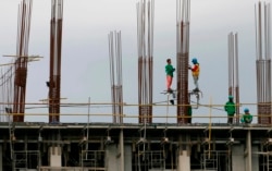 FILE - Construction workers stand on scaffolding around metal rods of a new pillar as they add more floors to a building project in suburban Paranaque city, south of Manila, Philippines, Jan. 26, 2017.