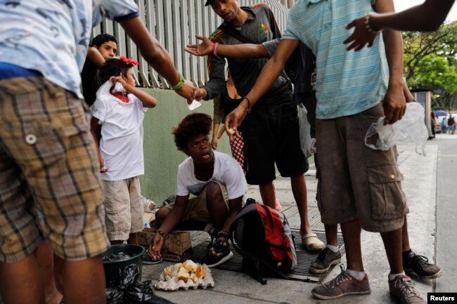 Youths eat a cake they'd found in a trash bag in Caracas, Venezuela, Feb. 27, 2019.