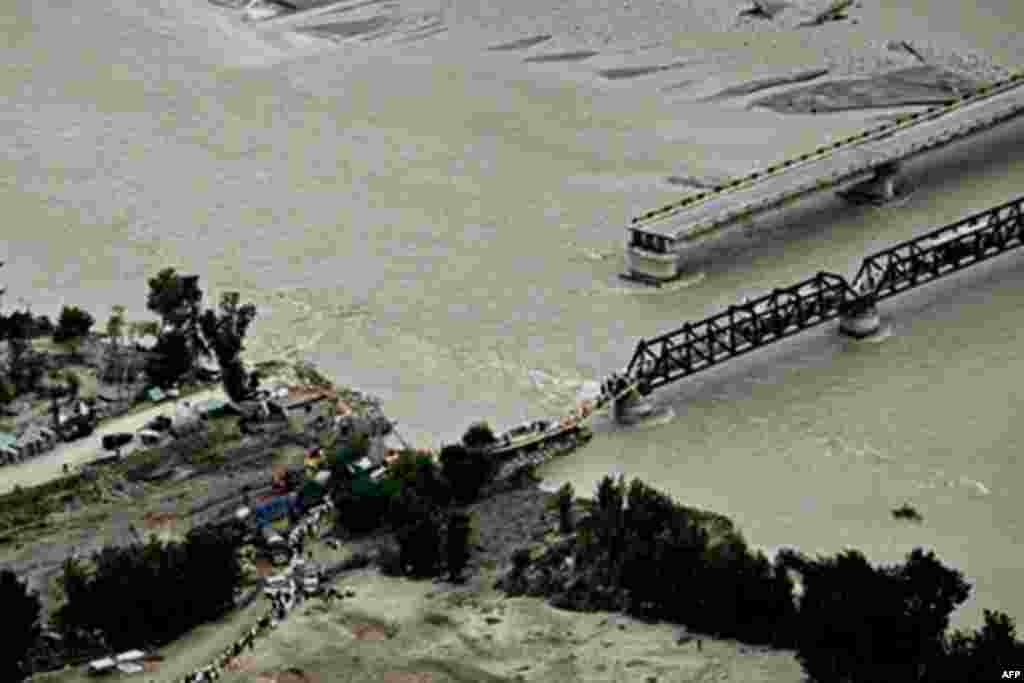 Pakistani flood survivors cross a hastily-repaired bridge next to a main bridge swept away by flood waters in Swat Valley, 10 Aug 2010