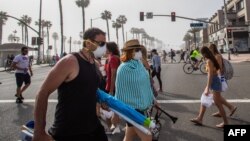 People cross the street, some wearing masks, amid the novel coronavirus pandemic in Huntington Beach, California on April 25, 2020. - Orange County is the only county in the area where beaches remain open, lifeguards in Huntington Beach expect tens of tho
