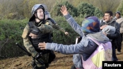 FILE - A Macedonian police officer hits a stranded migrant attempting to cross the Greek-Macedonian border, near Gevgelija, Macedonia, Dec. 2, 2015. 