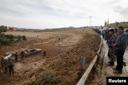 Warga setempat menyaksikan anggota pertahanan sipil melakukan pencarian korban pasca badai yang memicu banjir bandang, di kota Madaba, dekat Amman, Yordania, (10/11).