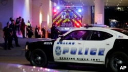 A Dallas police vehicle follows an ambulance carrying a patient to the Baylor University Medical Center, as police and others stand near the emergency entrance early Friday, July 8, 2016.