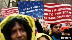 FILE - People hold signs before marching to Trump Tower in a protest organized by the New York Immigration Coalition against President-elect Donald Trump in New York, Dec. 18, 2016.