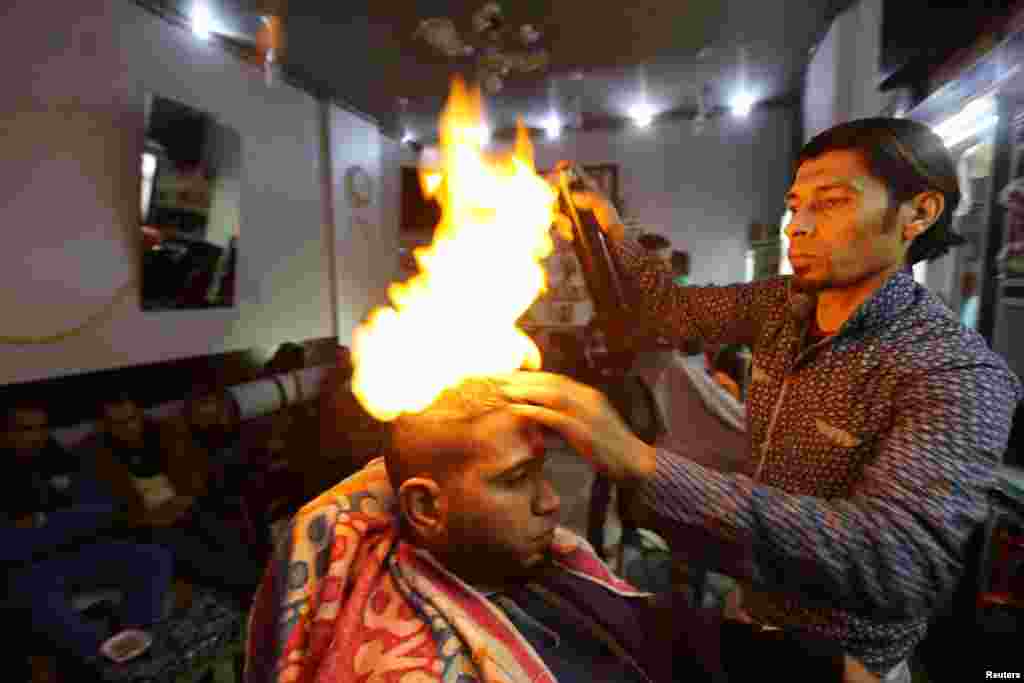 Tukang cukur Palestina, Ramadan Odwan, meluruskan dan membentuk rambut pelanggannya dengan api di salonnya di Rafah, Jalur Gaza.