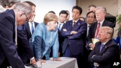  In this photo made available by the German Federal Government, German Chancellor Angela Merkel, center, speaks with U.S. President Donald Trump, seated at right, during the G7 Leaders Summit in La Malbaie, Quebec, Canada, on Saturday, June 9, 2018