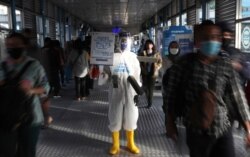 FILE - An employee wearing protective gear as a precaution against the new coronavirus holds a banner displaying information about the virus, at the Harmoni Central Busway station in Jakarta, July 16, 2020.
