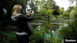 A woman takes pictures from the bridge at the nympheas pond garden as she visits the reopened Claude Monet house and foundation after restrictions to prevent the spread of COVID-19 were eased, in Giverny, France, June 9, 2020. (REUTERS/Benoit Tessier) 