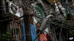 Seorang perempuan berdiri di balkon rumahnya yang berhimpitan dengan kabel-kabel listrik dan telepon yang bergantungan tidak teratur di wilayah Yangon, Burma (25/9). 