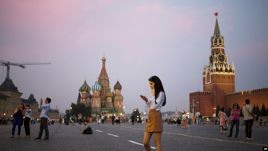 Seorang wanita muda memegang telepon genggamnya di Lapangan Merah dengan latar belakang Menara Spasskaya Kremlin (kanan) dan Katedral St. Basil (tengah) di latar belakang di Moskow, Rusia, Senin, 25 Juli 2016. (AP Photo / Pavel Golovkin)