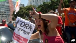 Seorang demonstran memegang kertas bertuliskan "Temer Out" dalam protes melawan Presiden Brazil Michel Temer di pantai Copacabana beach, Rio de Janeiro, Brazil (4/9). (AP/Silvia Izquierdo)