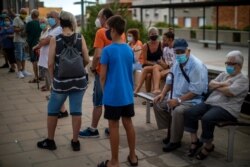 People wearing face masks wait their turn to be called for a PCR test for the COVID-19 outside a local clinic in Santa Coloma de Gramanet in Barcelona, Spain, Aug. 11, 2020.