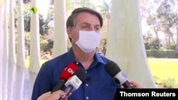 El presidente de Brasil, Jair Bolsonaro, habla con periodistas mientras usa una mascarilla. Foto Archivo.